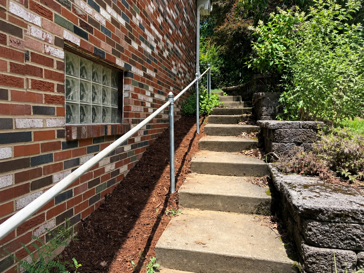 Fresh mulch installed along a concrete walkway and brick home